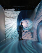 Person standing in the MIDEN VR immersive environment with images of water on the walls & floor.