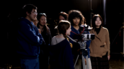 Group of students behind a video camera with a dark background.