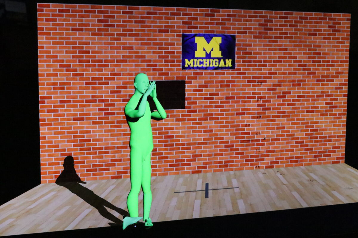 The green man figure in front of the brick background with Michigan logo