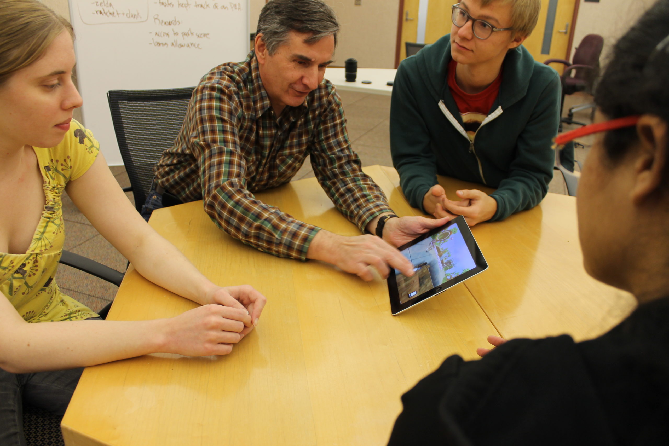 Ted holding an IPad talking with the other three students